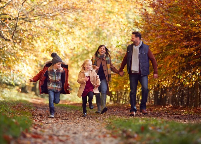 Family Walking Along Track In Autumn Countryside With Children Running Ahead