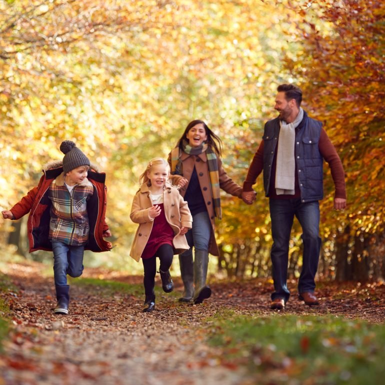 Family Walking Along Track In Autumn Countryside With Children Running Ahead